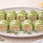 Finished Cucumber Rolls filled with smoked salmon and cream cheese, sliced into bite sized pinwheels and served on a white plate with dill and sesame seeds.